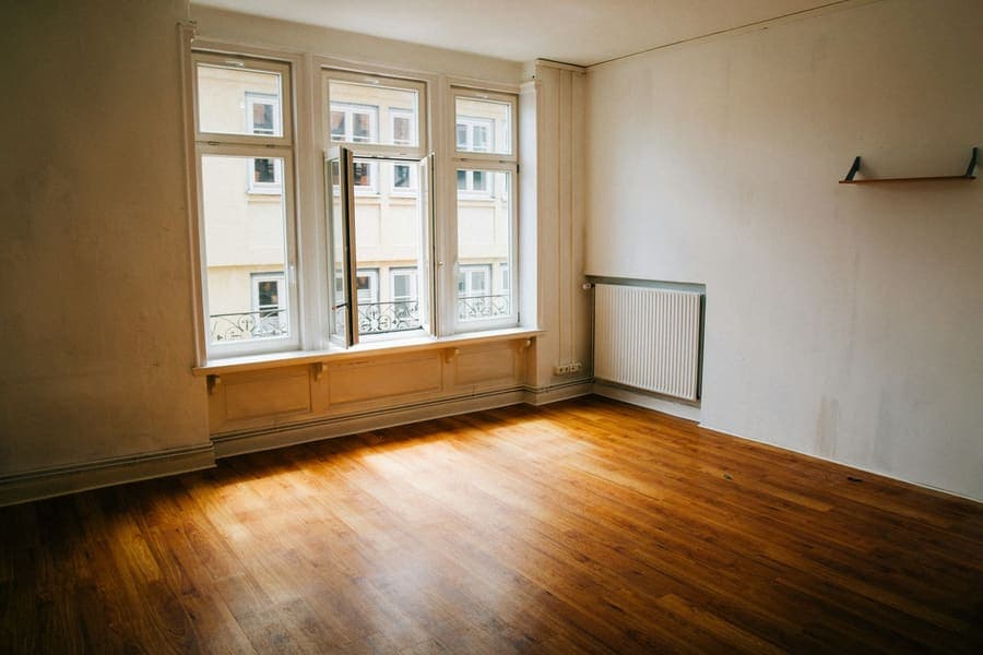 Pièce vide au parquet foncé, fenêtres et radiateur