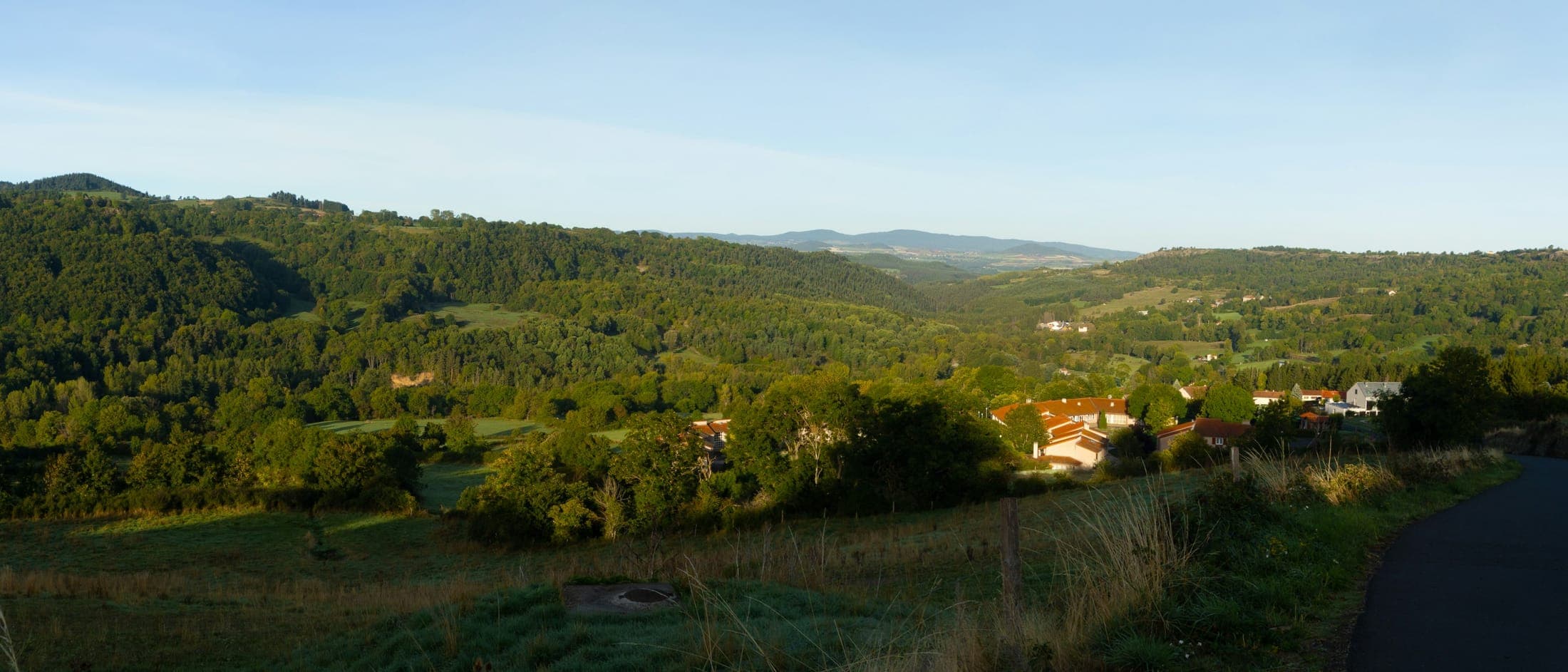 Vallée boisée et village aux toits de tuiles, lumière du soir